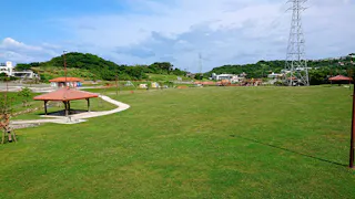 A large open grassy park with a red-roofed gazebo, walking paths, distant playground equipment, power lines, and green hills under a partly cloudy sky.