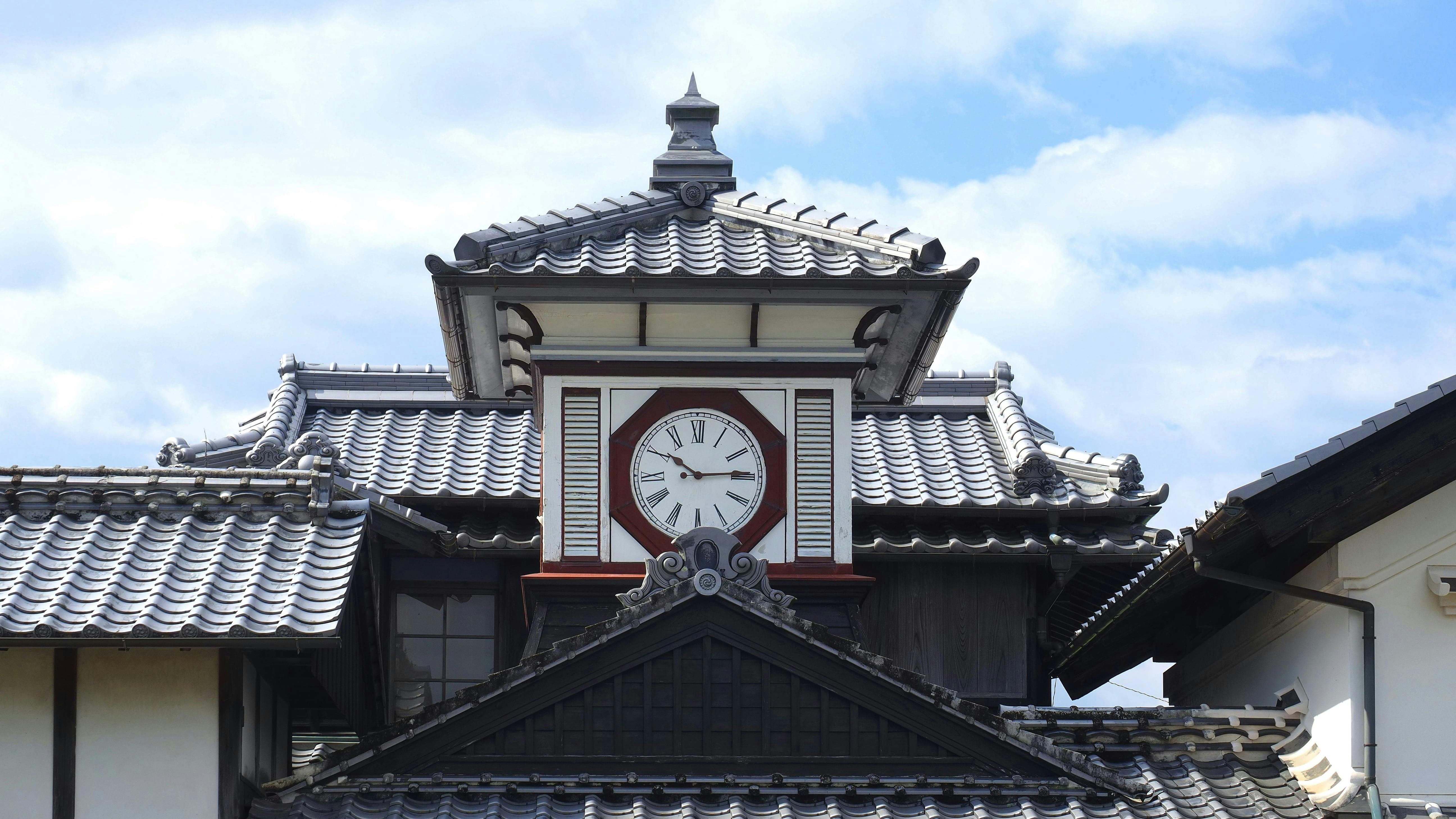 Traditional Japanese building with a tiled roof and a large round clock centered on the upper facade; the sky is partly cloudy in the background.