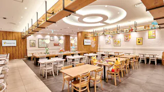 A brightly lit Pokémon-themed café with wooden tables and chairs, featuring Pokémon plush toys and character artwork on the walls. Shelves display colorful Pokémon figures, creating a playful and inviting atmosphere.