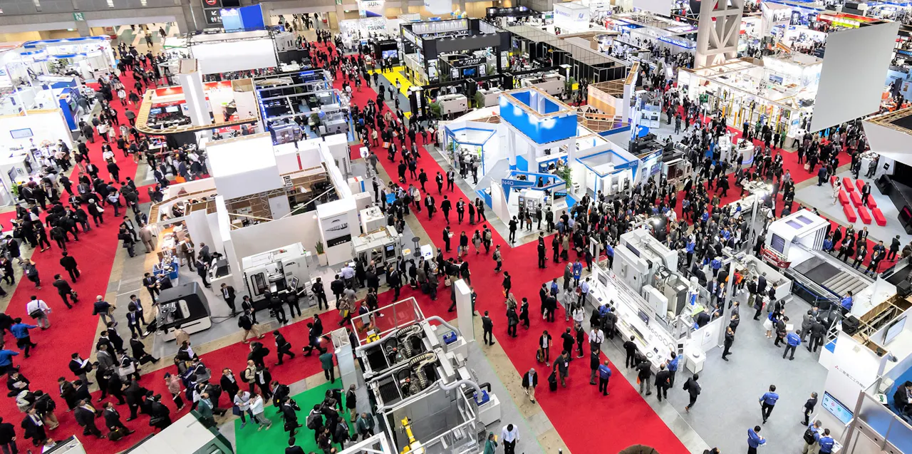 Tokyo Big Sight's exhibition halls fill with booths and crowds during major events. A packed exhibition hall at Tokyo Big Sight seen from above, with crowds walking between rows of booths on red carpet