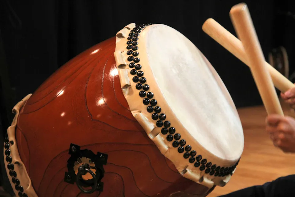 Los palillos de un tamborilero levantados sobre la cabeza de un gran tambor taiko de madera