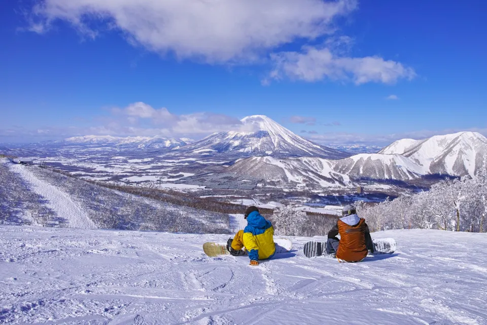 Snowboarders taking a break at Rusutsu Ski Resort in mid-winter, gazing at Mount Yotei