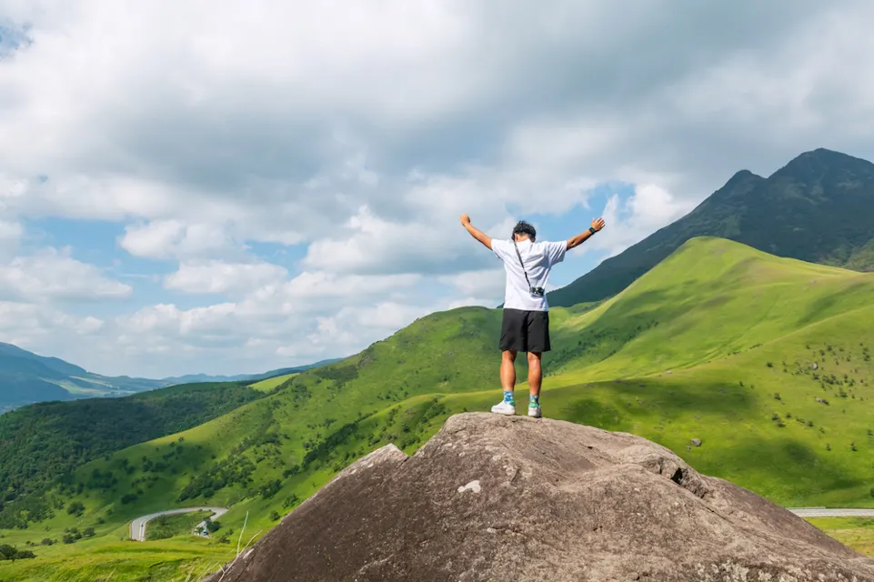 Japanese man on a hilltop with arms raised near Mt. Yufu, Yufuin, Oita, Japan