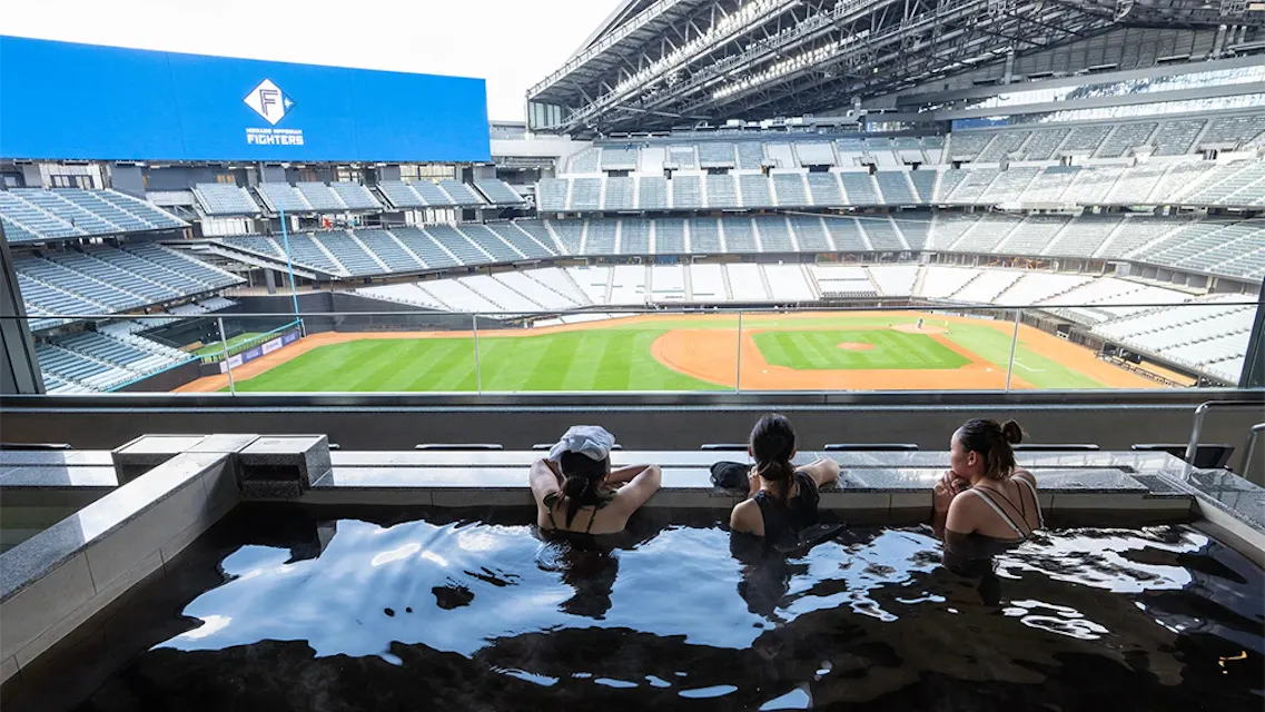 tower eleven onsen looks directly onto the field, with a swimsuit zone open on game days and non-game days Three bathers sit in the tower eleven hot spring pool looking out over the empty green playing field at Es Con Field