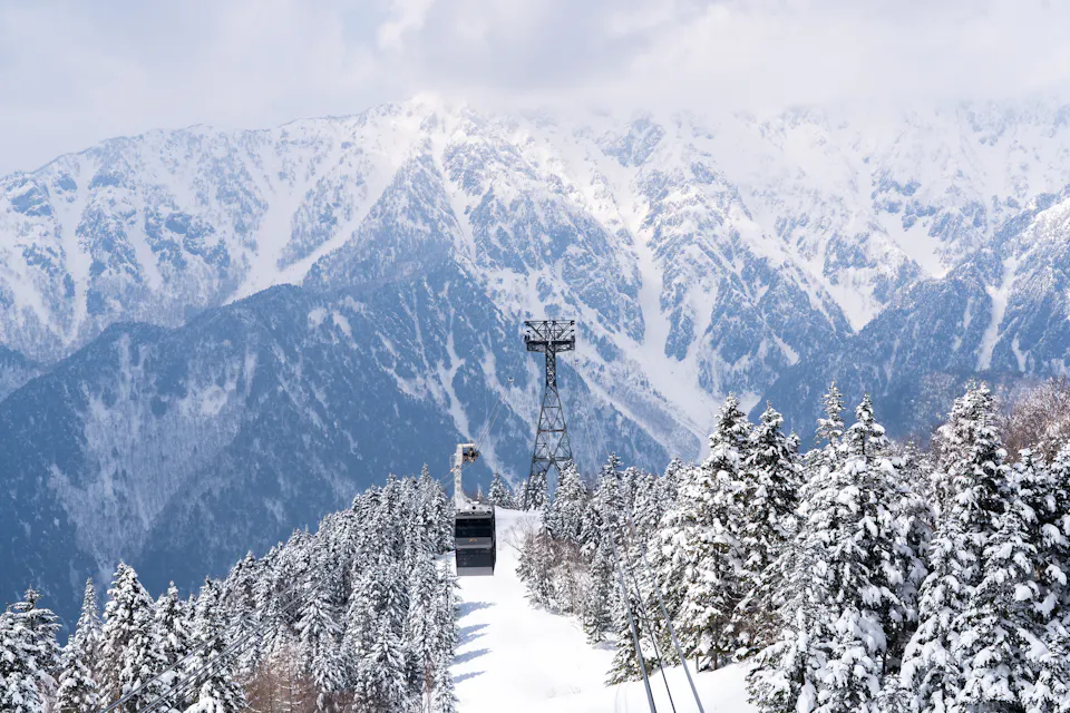 The Shin-Hotaka Ropeway climbs to views of the Northern Alps above Okuhida Onsengo. A Shin-Hotaka Ropeway gondola rising over snow-covered forest toward jagged white Alpine peaks