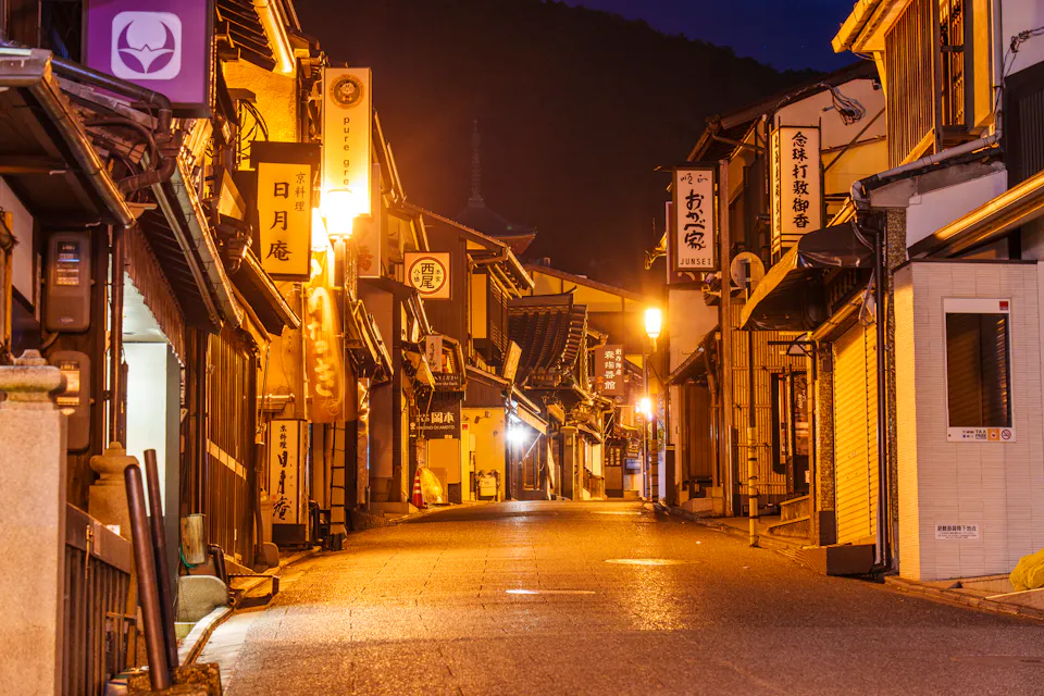 京都夜晚，一条狭窄的街道，两侧是灯火通明的木质店面和悬挂的招牌