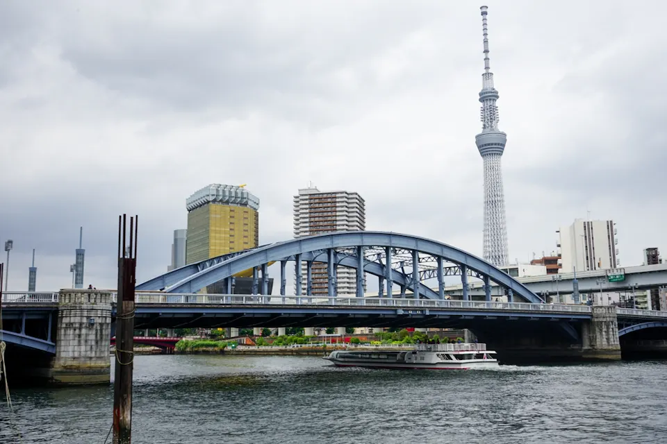 隅田川に架かる駒形橋と、その背後に見える東京スカイツリー。 曇り空の下、青いアーチ型の駒形橋が隅田川に架かり、その背後に東京スカイツリーがそびえ立つ