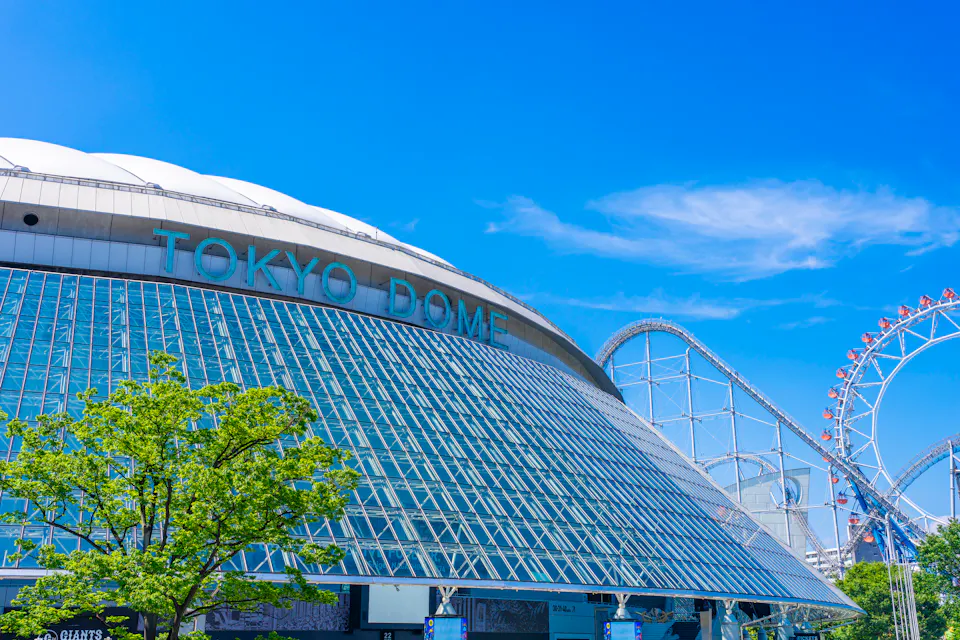 Tokyo Dome, home of the Yomiuri Giants and the easiest first game in Tokyo The glass and white-roofed exterior of Tokyo Dome with a roller coaster track curving behind it against a blue sky