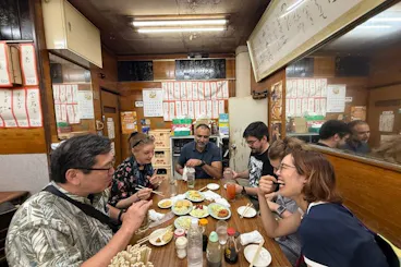 Tour group sharing food and drinks around a table in a traditional izakaya during an Osaka Kyobashi bar-hopping night tour
