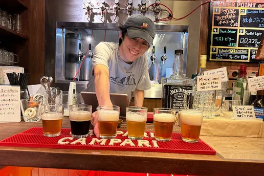 Smiling bartender presenting a flight of six craft beer tasting glasses at an Osaka beer bar