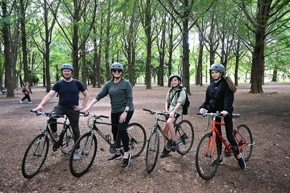 緑豊かな公園の小道を探検する準備が整った家族。 渋谷のサイクリングツアーで、東京の公園にある緑豊かな森の小道に自転車と並んで立つ家族