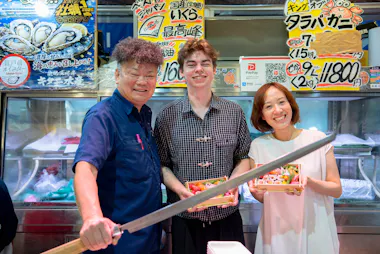Tour guests posing with a Tsukiji Outer Market fishmonger holding a large tuna knife on the Tokyo sushi food tour