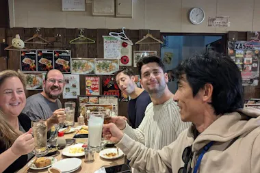 Tour group toasting drinks with their local guide at a cozy izakaya on an Osaka Namba food tour
