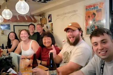 Group of guests and a local host smiling around a table of beer bottles under vintage posters in an Osaka izakaya
