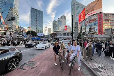 Cyclists posing with bikes near the Shibuya Station crossroads at dusk on a Tokyo Shibuya cycling tour