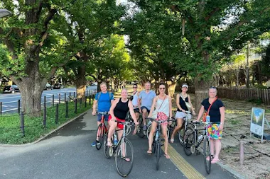 Cycling group resting under leafy green trees along a tree-lined avenue on a Tokyo Shibuya bike tour