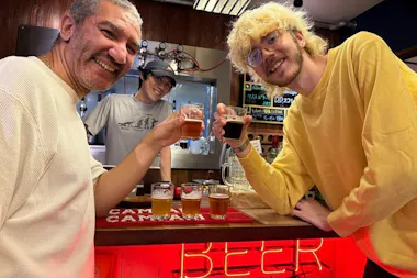 Two guests toasting small craft beer tasting glasses under a red BEER neon sign in Osaka