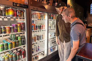 Two guests browsing a fridge stocked with colourful Japanese craft beer cans in Osaka