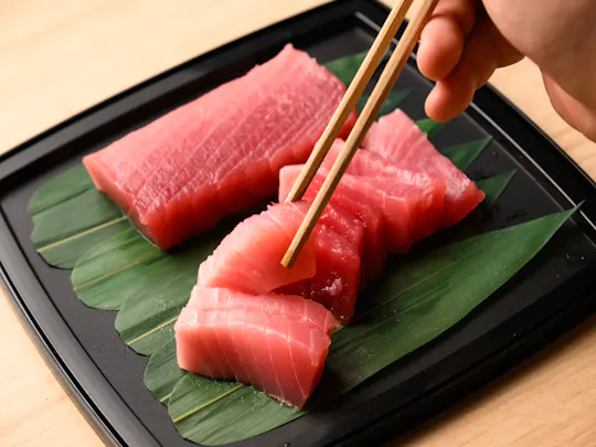 Chopsticks lifting a slice of fresh maguro tuna sashimi from a black tray on the Tsukiji food tour in Tokyo