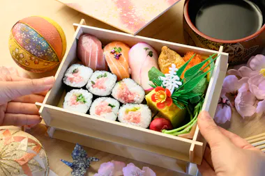 Overhead view of a wooden sushi box with nigiri, tuna rolls and tamago beside green tea at the Tokyo sushi class