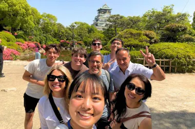 Smiling tour group taking a selfie in the Osaka Castle garden with the castle keep behind them