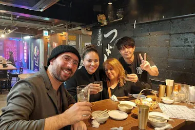 Guide and travelers toasting with drinks at an izakaya table on an Osaka Kyobashi bar-hopping tour