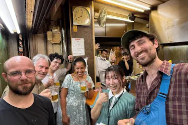 Travelers holding beers in the doorway of a local izakaya on an Osaka Kyobashi bar-hopping night tour
