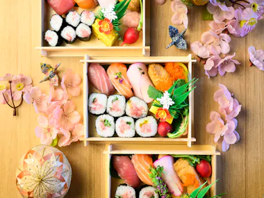 Several handmade sushi bento boxes arranged with cherry blossoms and temari balls, seen from above