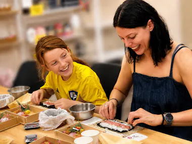 A woman and a child laughing while rolling sushi together at a Tokyo sushi-making class