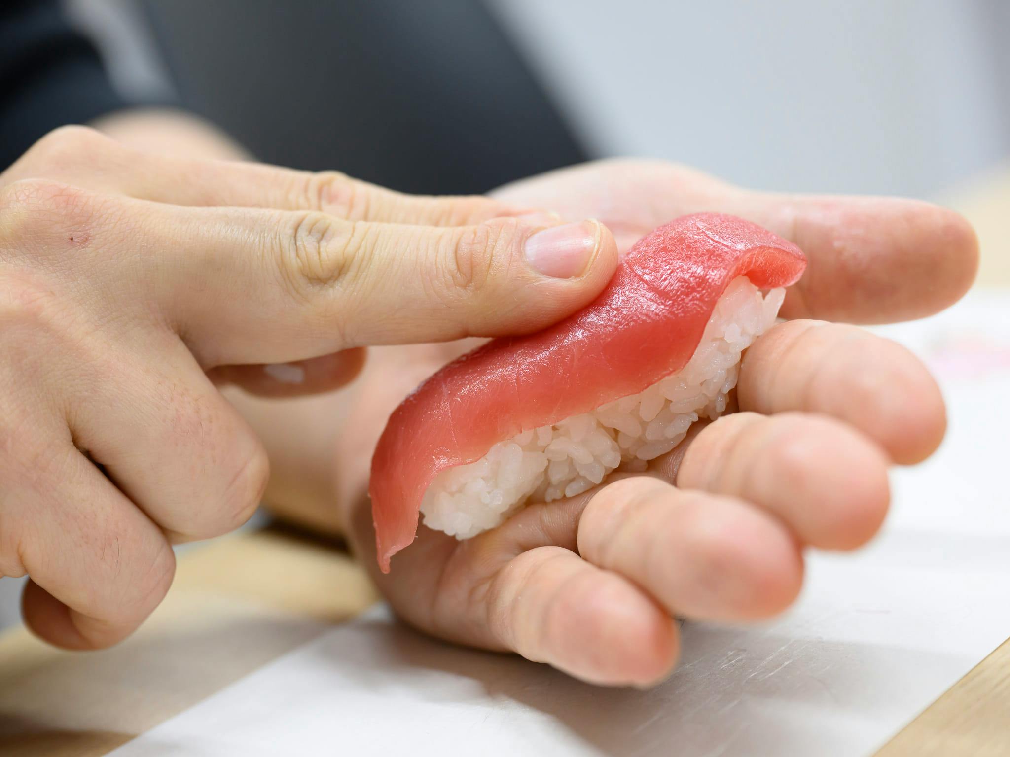 Hands shaping a piece of tuna nigiri sushi over seasoned sushi rice