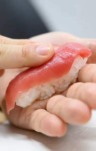 Forming tuna nigiri with guidance from the chef Hands shaping a piece of tuna nigiri sushi over seasoned sushi rice