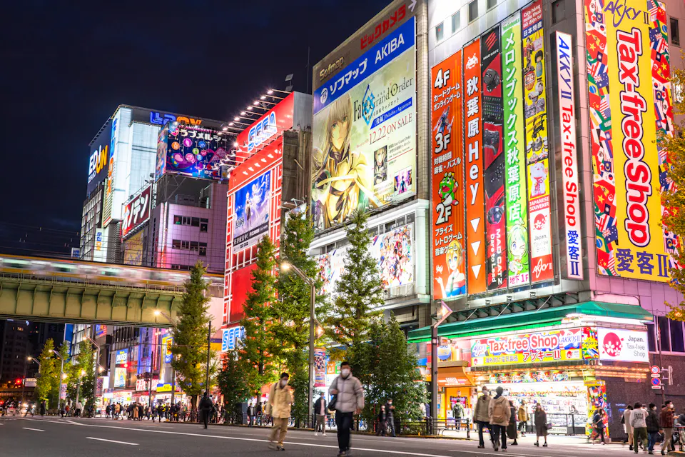 Akihabara is Tokyo's main district for anime, game and figure shops. Akihabara's main street at dusk, lined with tall buildings covered in colorful anime and game advertising signs