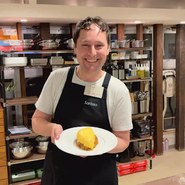 Showing off a freshly made omurice. Guest holding a plate of omurice in a cooking studio lined with shelves of cookware