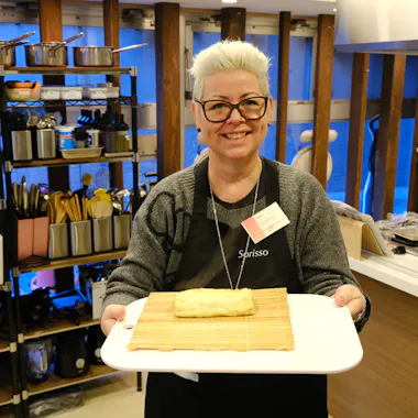 A finished tamagoyaki, ready to slice. Guest holding a freshly made tamagoyaki rolled omelet on a bamboo mat