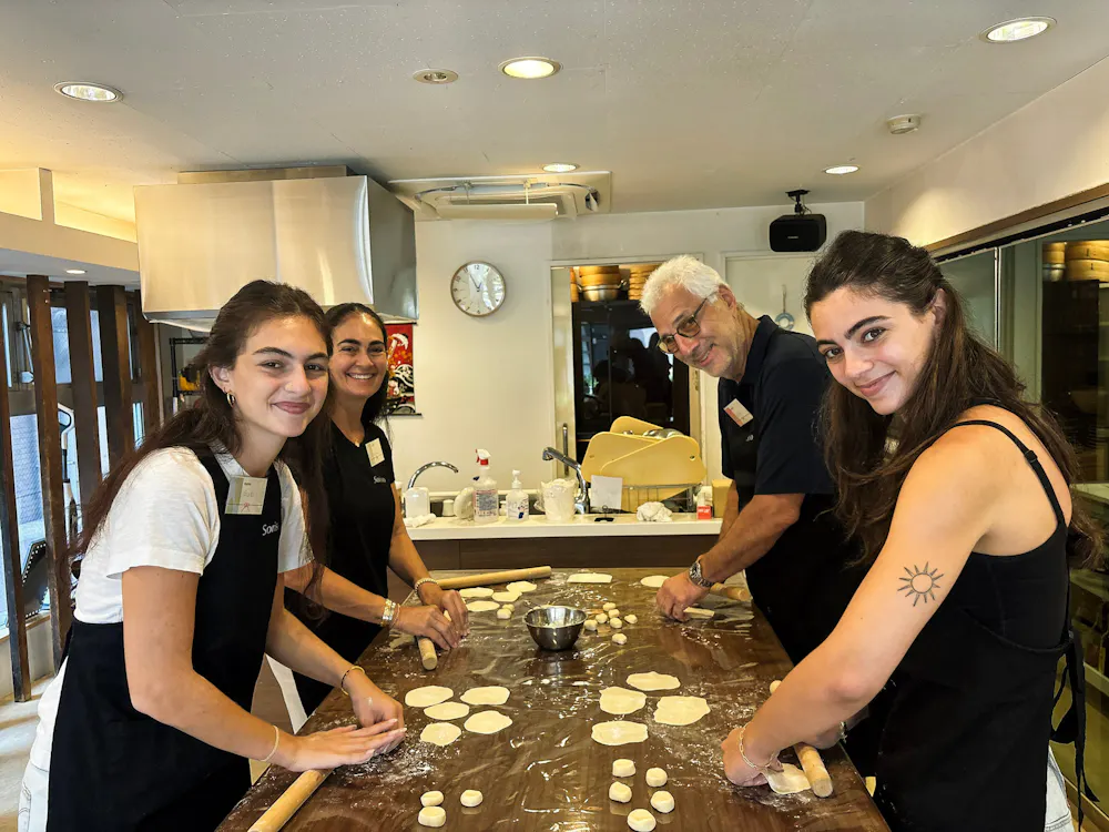 Working the dough at the studio's long counter. Guests rolling dough into gyoza wrappers around a long kitchen counter in Ebisu