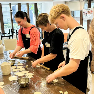 A small group gets hands-on with the dough. Group of travelers preparing gyoza wrappers together at a Tokyo cooking class