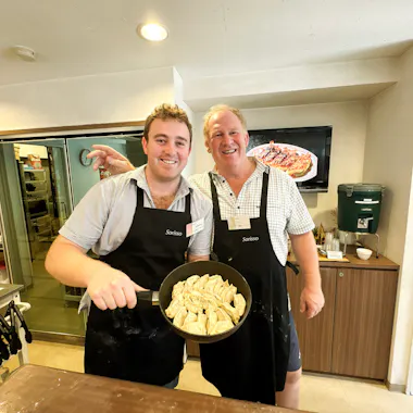 A full pan of gyoza ready to serve. Two guests holding a frying pan of freshly cooked gyoza in a cooking studio