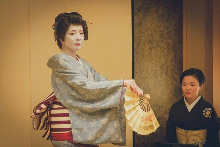 Asakusa geisha dancing with a folding fan beside a woman in dark kimono in a tatami room