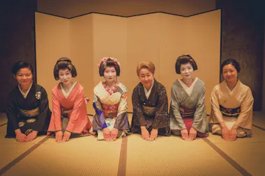 Okami and geisha kneeling in a row to welcome guests in a tatami room