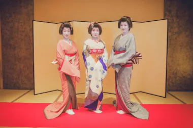 Three geisha in colorful kimono standing before a gold folding screen