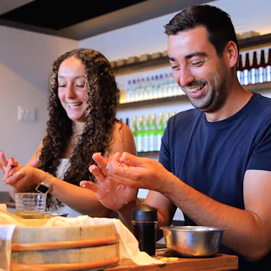 A couple's private sushi lesson. Couple pressing nigiri rice with big smiles at a sushi table