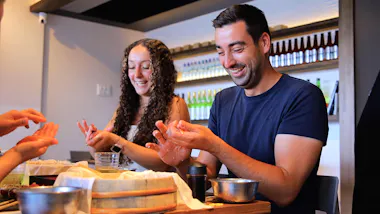 Couple pressing nigiri rice with big smiles at a sushi table