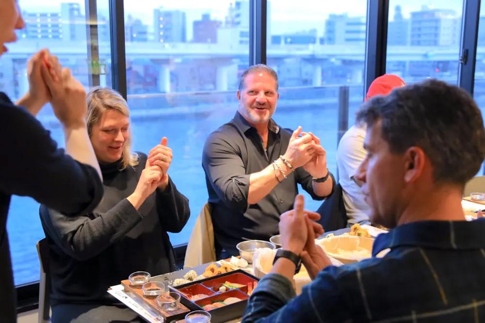 Group fun at the Tokyo class, with the river outside. Group of guests clapping along at a sushi class with river views in Tokyo