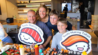 Family holding sushi mascot signs over a table of homemade rolls