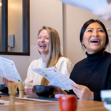 Learning matcha's story. Two women laughing as they read about matcha at the table