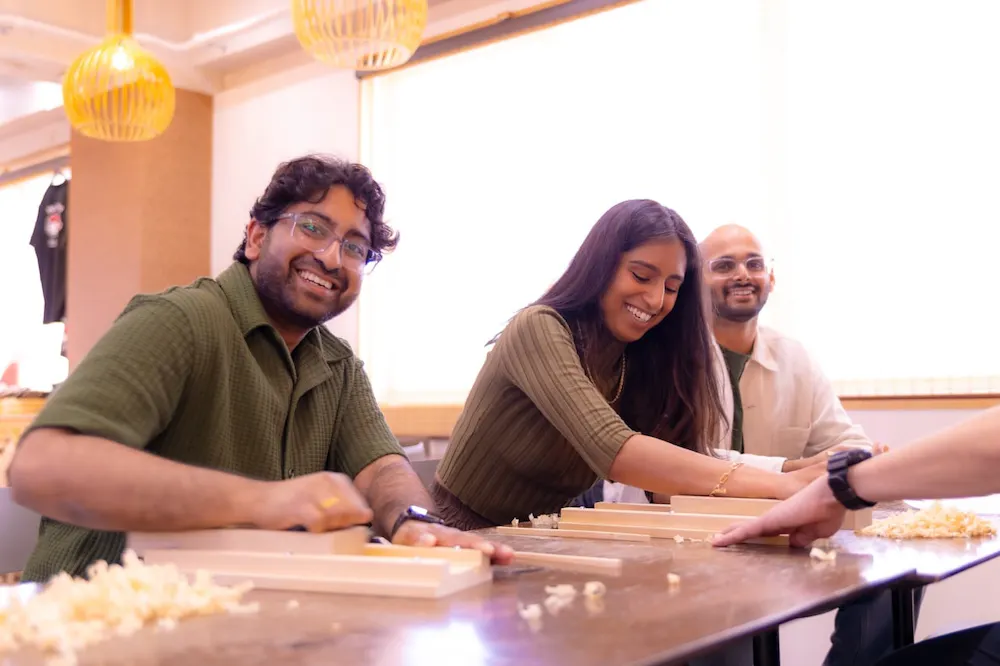 Three guests planing chopsticks at a long workshop table