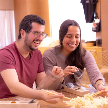 Laughter and wood shavings. Two guests laughing as they plane chopstick blanks at a wooden table