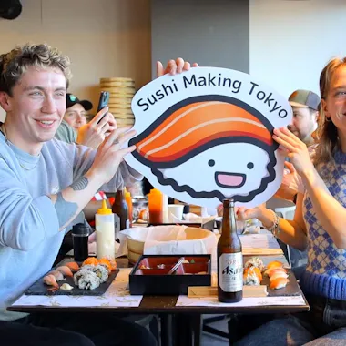Celebrating a finished tray of sushi in Asakusa. Travelers holding a Sushi Making Tokyo sign beside their finished sushi in Asakusa