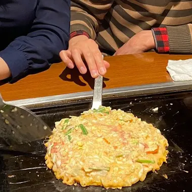 Attempting the flip on the hot plate. Guest flipping a savory pancake on an izakaya hot plate