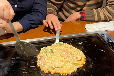 Guest flipping a savory pancake on an izakaya hot plate